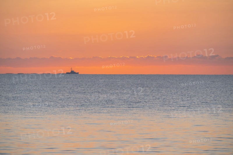 Calm sea at sunrise with fishing boat in distance