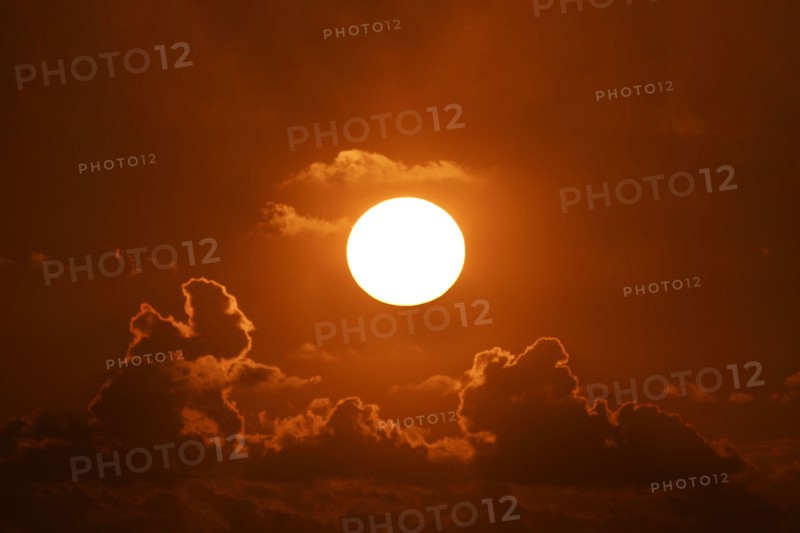 Bright sun at sunset with clouds against orange sky