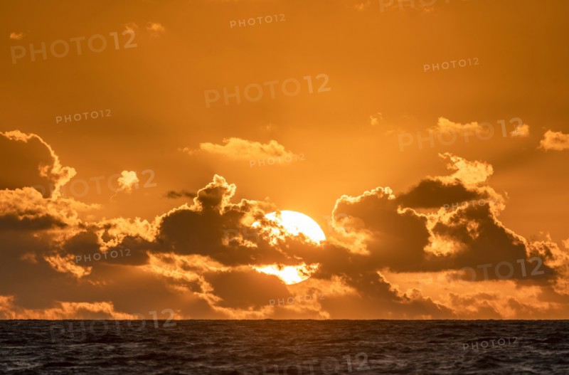 Sun behind clouds rising over ocean