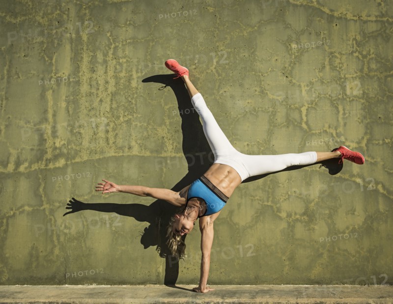 Athlete woman performing cart wheel against wall