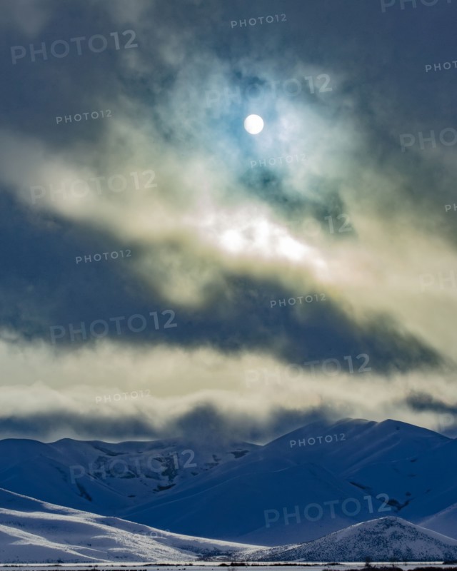 Sun shining through clouds above snowcapped mountains