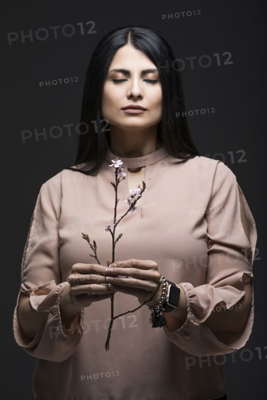 Studio portrait of woman holding blooming twig with eyes closed