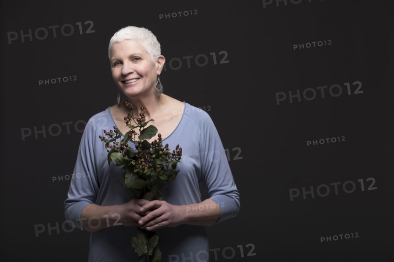Studio portrait of smiling woman in blue shirt holding bunch of flowers
