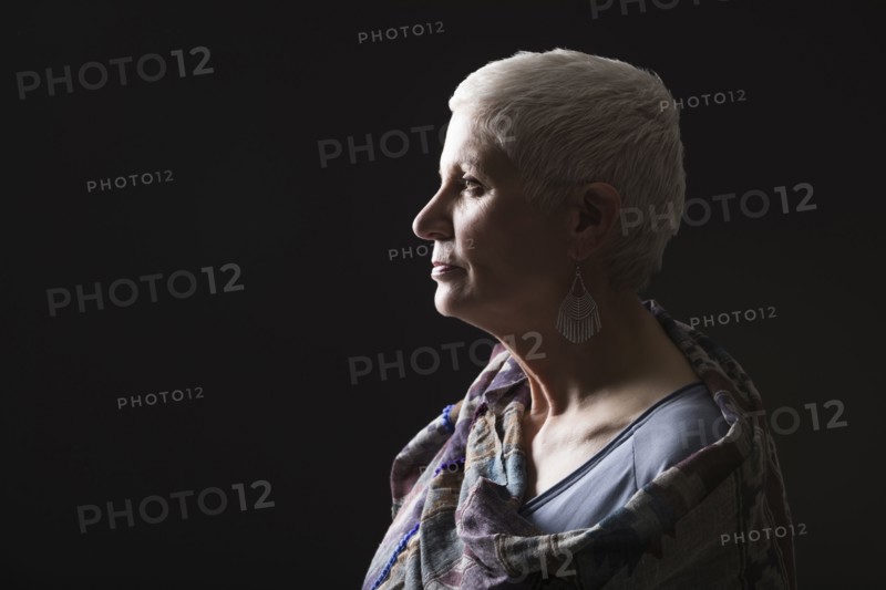 Profile of woman with white short hair wrapped in shawl against black background