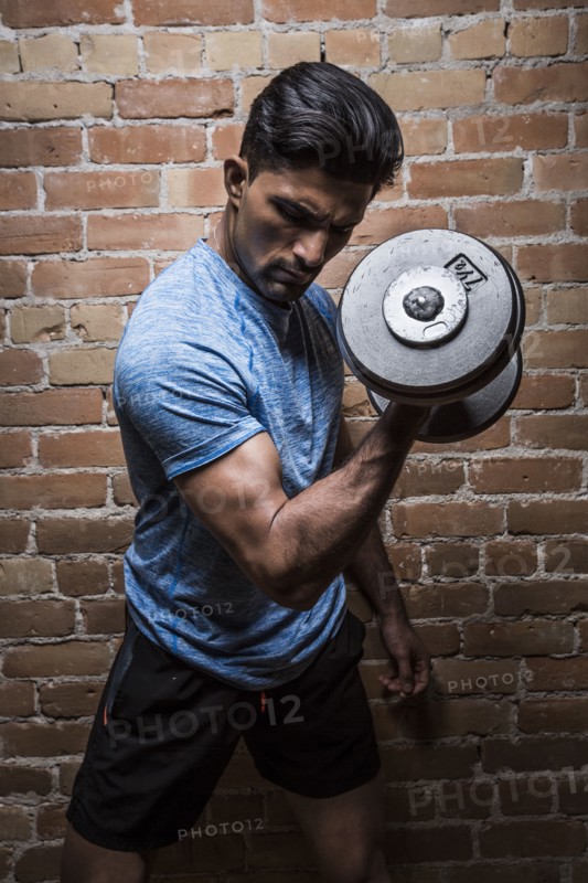 Man exercising with dumbbell against brick wall
