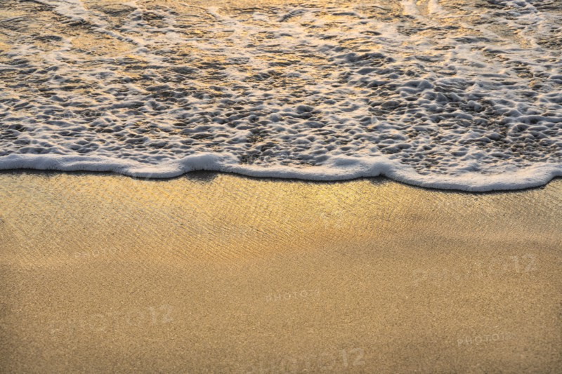 Close-up of ocean wave on sand at sunset