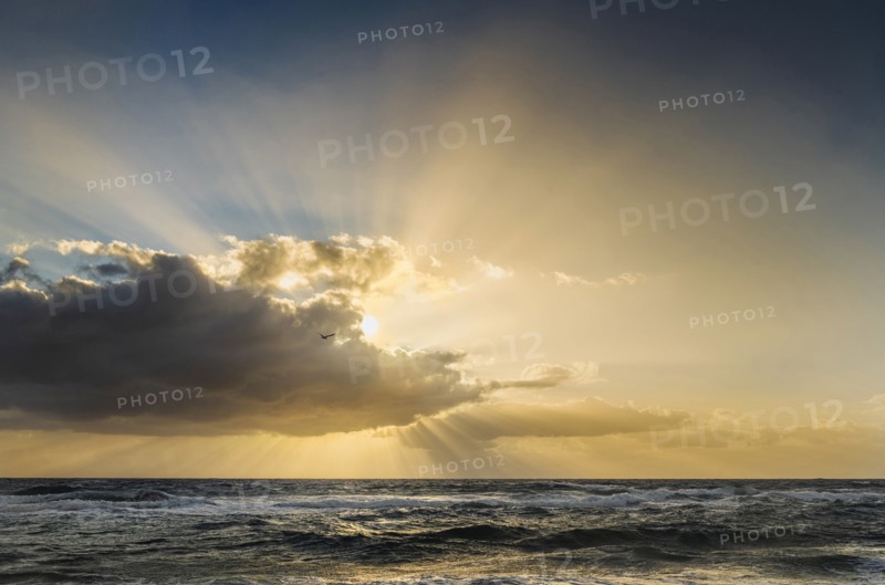 Sun rays bursting from behind clouds above sea at sunrise