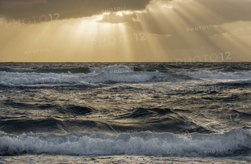Sun rays streaking from clouds over ocean waves