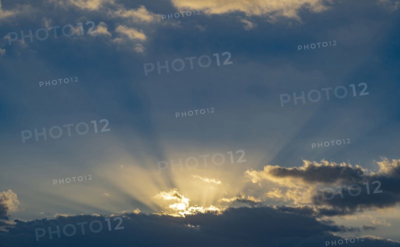 Sun rays streaking upwards from clouds against sky