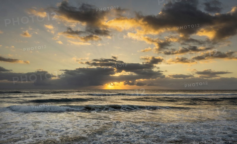 Ocean and dramatic golden streaks from morning clouds