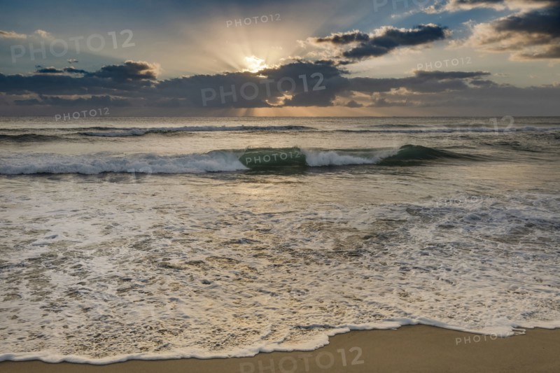 Rising sun shining through clouds above ocean