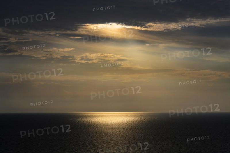 Sun shining through storm clouds and reflecting in ocean surface