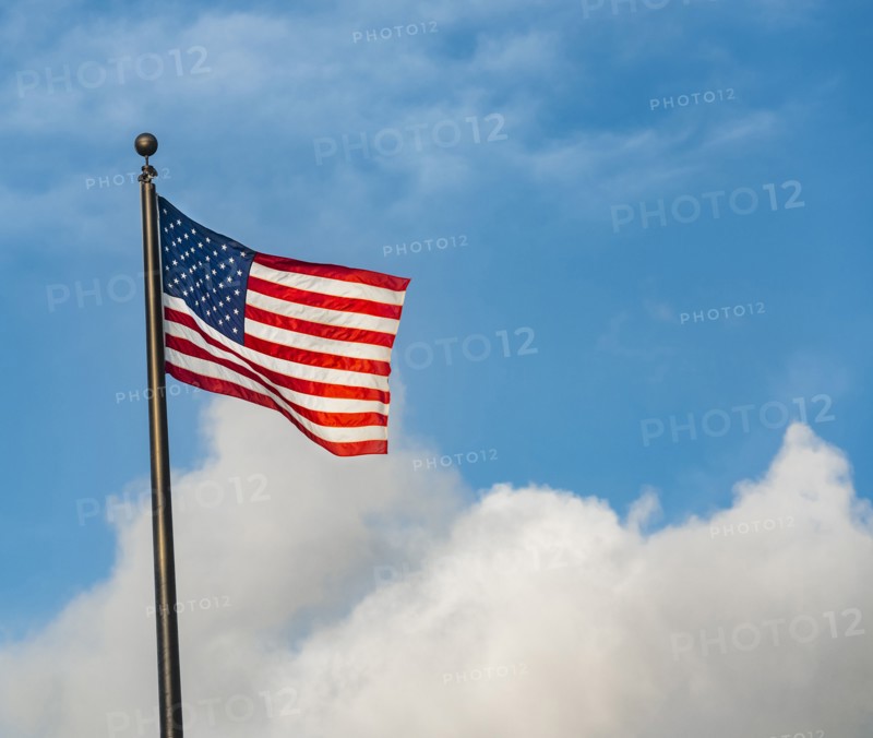 American flag on flag pole against cloudy blue sky
