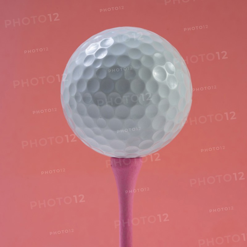 Golf ball on tee against pink background