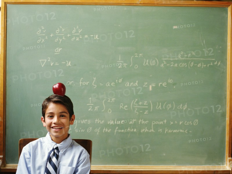 Portrait of boy (12-13) with apple on head sitting in front of chalkboard