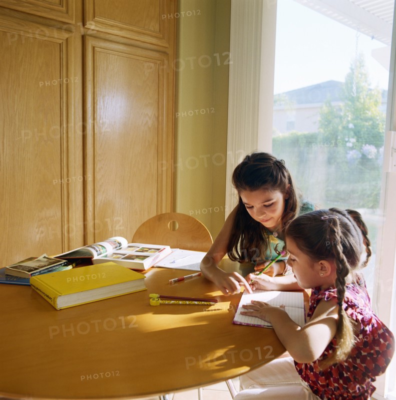 Two girls (10-11) doing homework at kitchen table