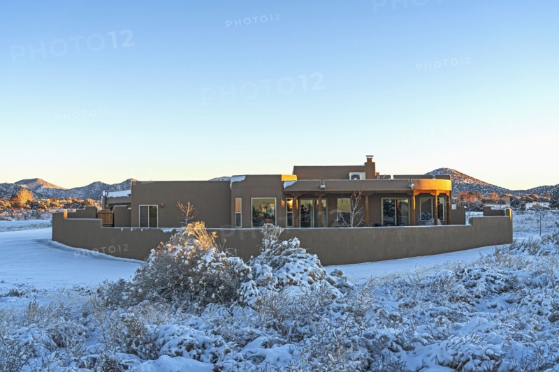 Pueblo style house in snow covered landscape at sunset