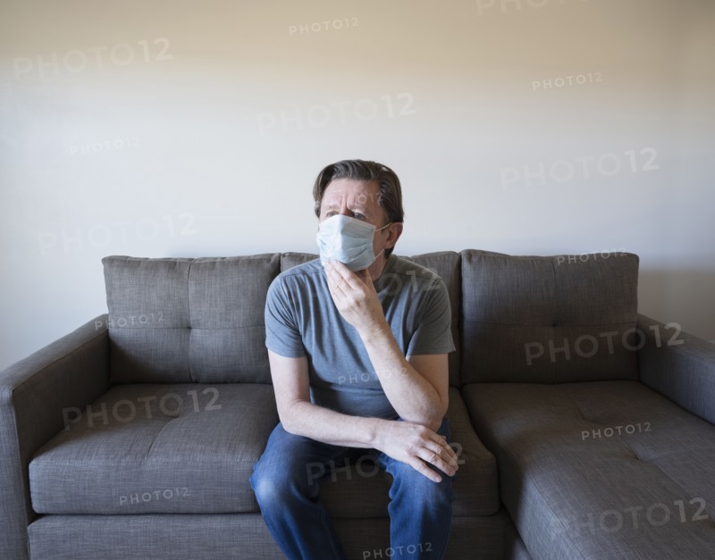 Pensive man in face mask sitting on sofa
