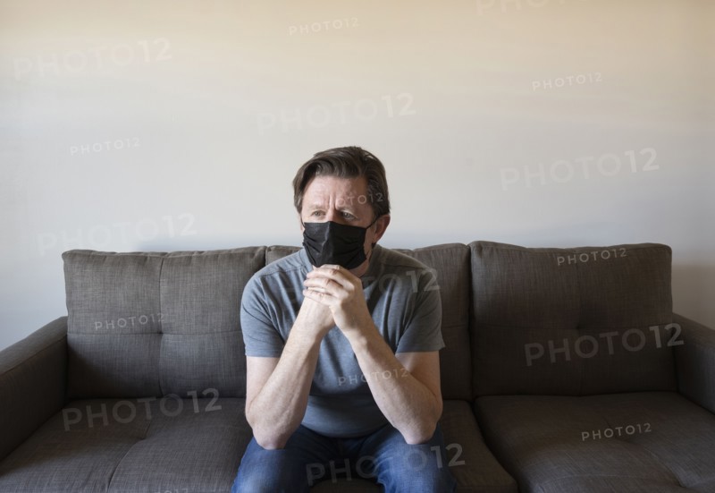 Pensive man in face mask sitting on sofa