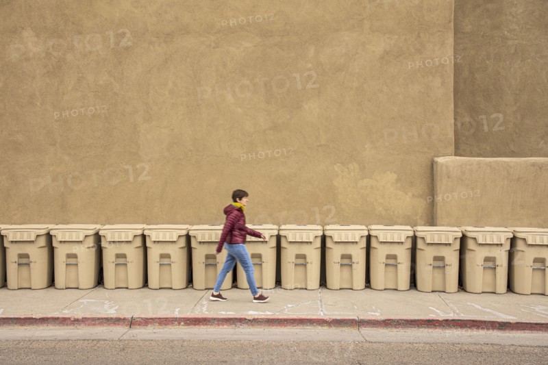 USA, New Mexico, Santa Fe, Woman walking past row of garbage bins
