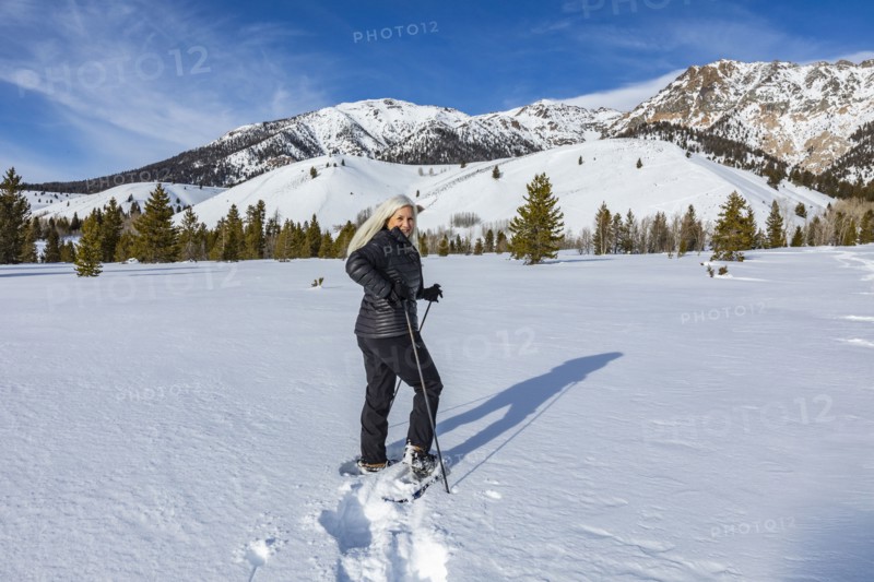 Senior blonde woman snow shoeing in snow covered landscape