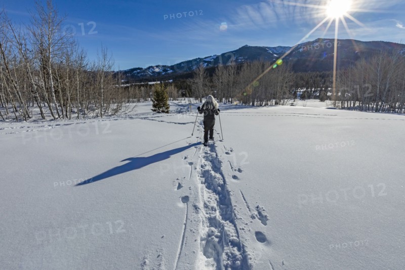 Rear view of senior blonde woman snow shoeing in snow covered landscape