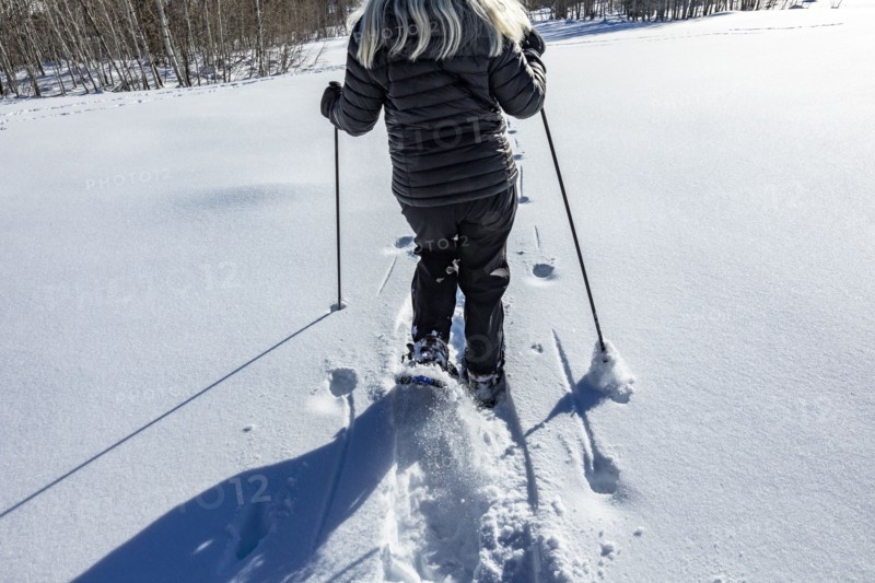 Rear view of senior woman snow shoeing in snow covered field