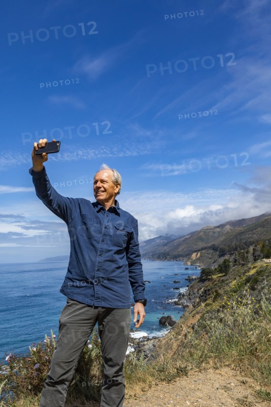 Smiling senior man taking selfie at Big Sur coast