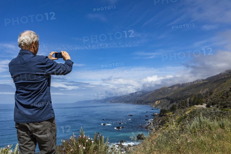 Rear view of senior man photographing Big Sur coast