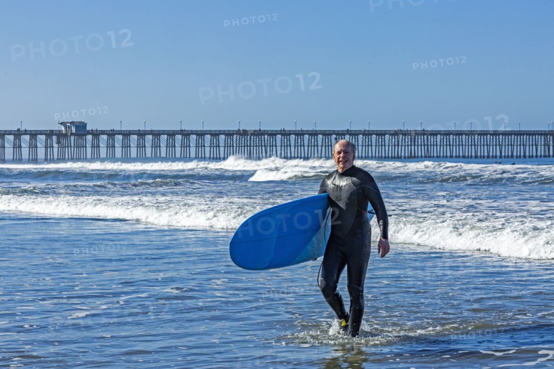 USA, California, Oceanside, Senior surfer carrying surfboard