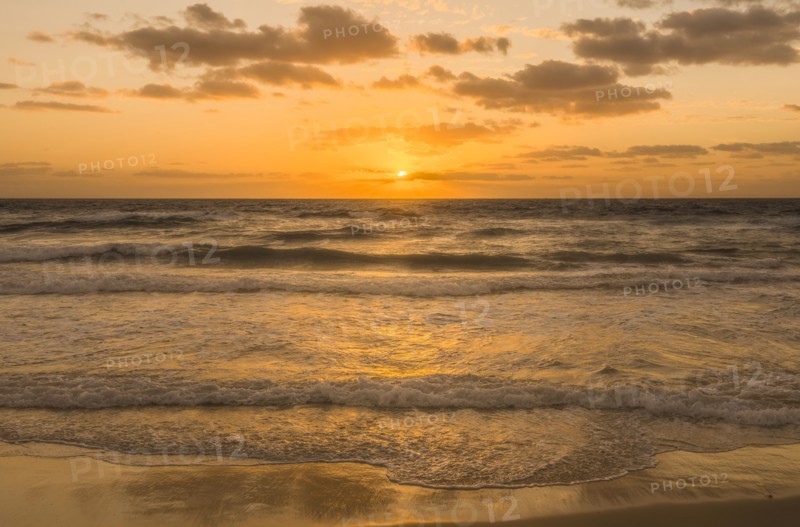 Golden sky with sun and calm ocean at sunset