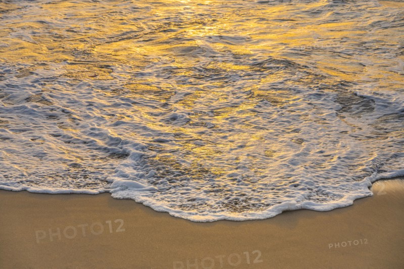 Close-up of calm ocean surf washing up onto beach at sunset