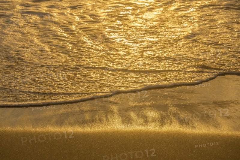 Close-up of calm ocean surf washing up onto beach at sunset