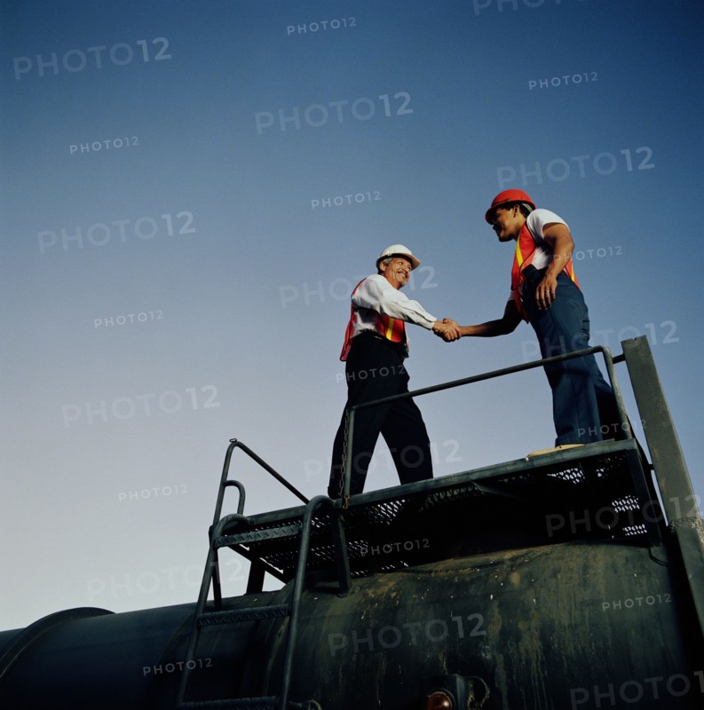 Two workers shaking hands on industrial platform
