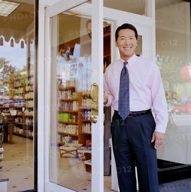 Portrait of store owner opening door to pharmacy