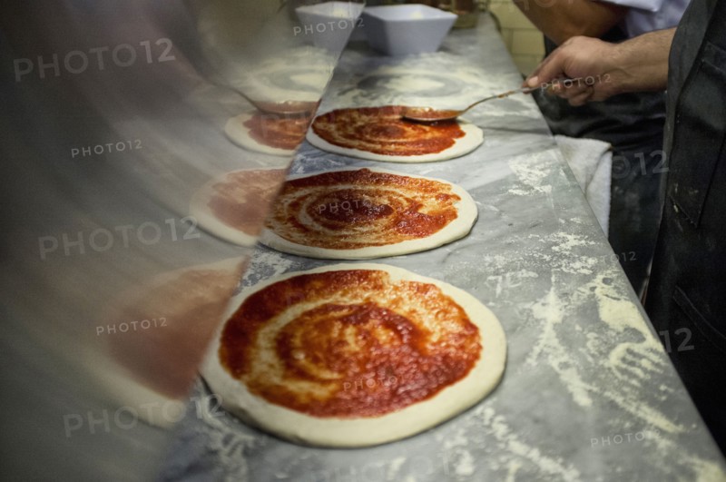 Man putting tomato sauce onto fresh hand made pizzas