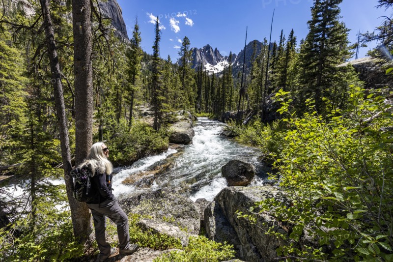 Senior blonde woman hiking by rushing stream in mountains near Sun Valley