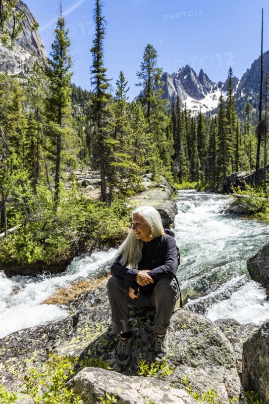 Senior blonde woman hiking by rushing stream in mountains near Sun Valley