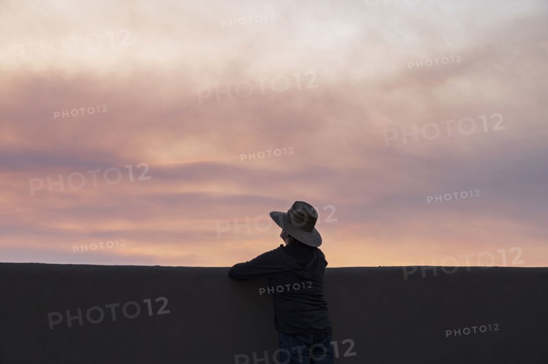 Rear view of man looking at wildfire smoke at sunset