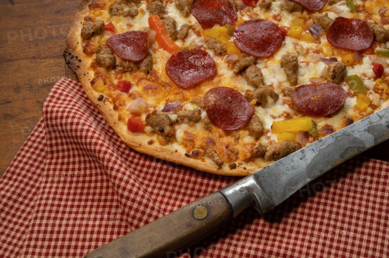 Pizza on wooden table with antique knife and red check cloth
