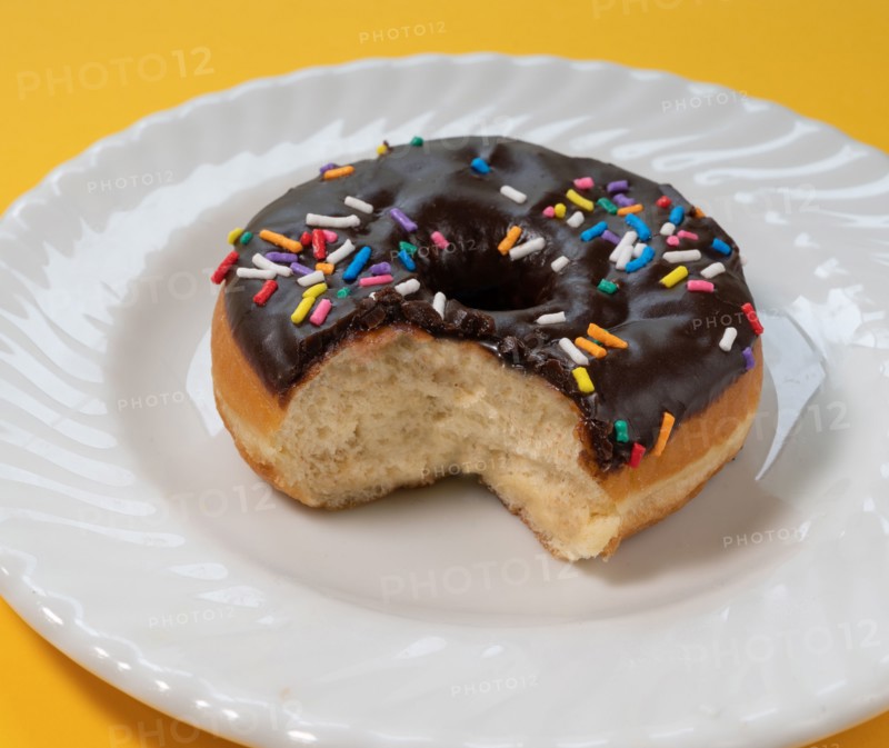 Eaten donut with chocolate icing and sprinkles on white plate