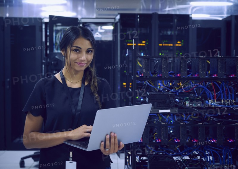 Portrait of smiling female technician using laptop in server room