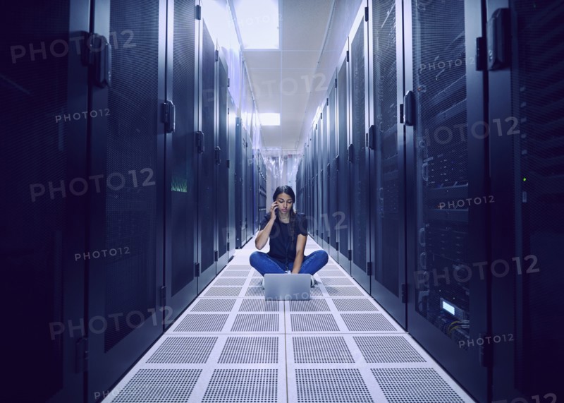 Female technician using laptop and smart phone on floor in server room