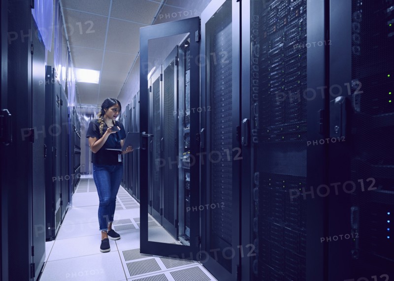 Female technician using smart phone and laptop in server room