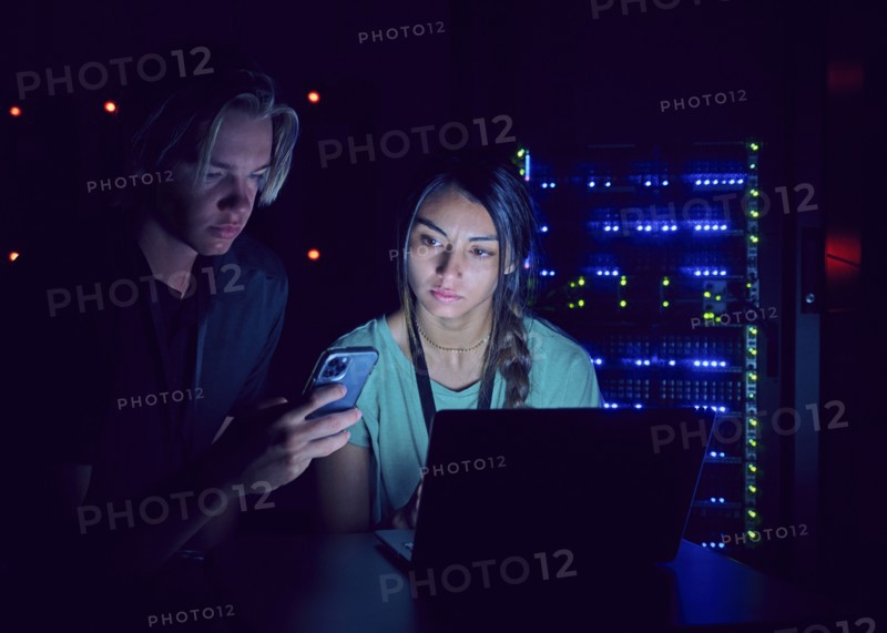 Technicians using laptop and smart phone in server room