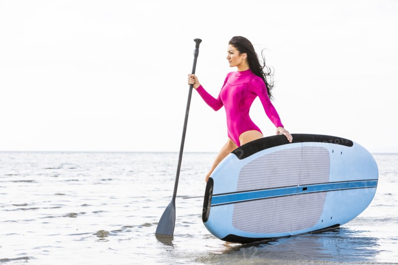 Woman in pink swimsuit standing with paddleboard by lake