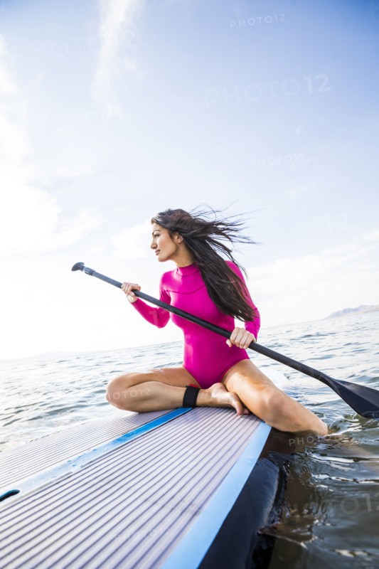 Woman in pink swimsuit sitting on paddleboard on lake