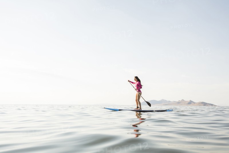 Woman in pink swimsuit paddleboarding on lake