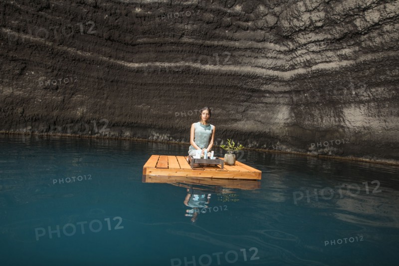 Beautiful woman kneeling on wooden raft on pond