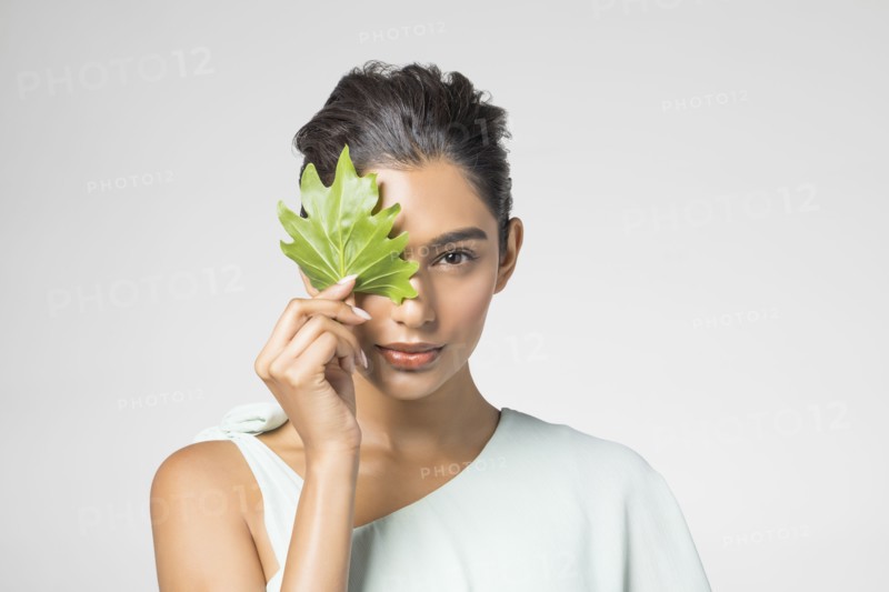 Studio portrait of beautiful woman with leaf on her face